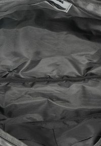 Interno della borsa in nylon nera, con una texture liscia, un singolo compartimento e una fodera morbida con una banda elastica al centro.