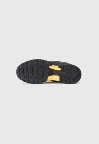 Semelle de sneaker noire en caoutchouc texturé, avec des accents jaunes. Le motif de la semelle comprend des designs rectangulaires et circulaires pour une meilleure adhérence.
