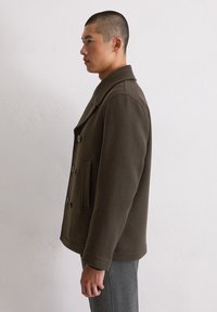 Brązowy wełniany płaszcz typu peacoat z wyłogowym kołnierzem, podwójnym zapięciem na guziki i kieszeniami po bokach. Gładka tekstura z dopasowanym krojem.