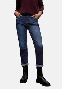 Jeans de mezclilla azul medio con un ajuste clásico, que presentan puños doblados y un diseño de cinco bolsillos, combinados con botines negros.