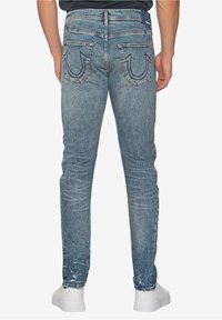 Úzké džíny světle modré denimové barvy, s vybledlou texturou, charakteristickými zadními kapsami s prošitím a středním pasem.