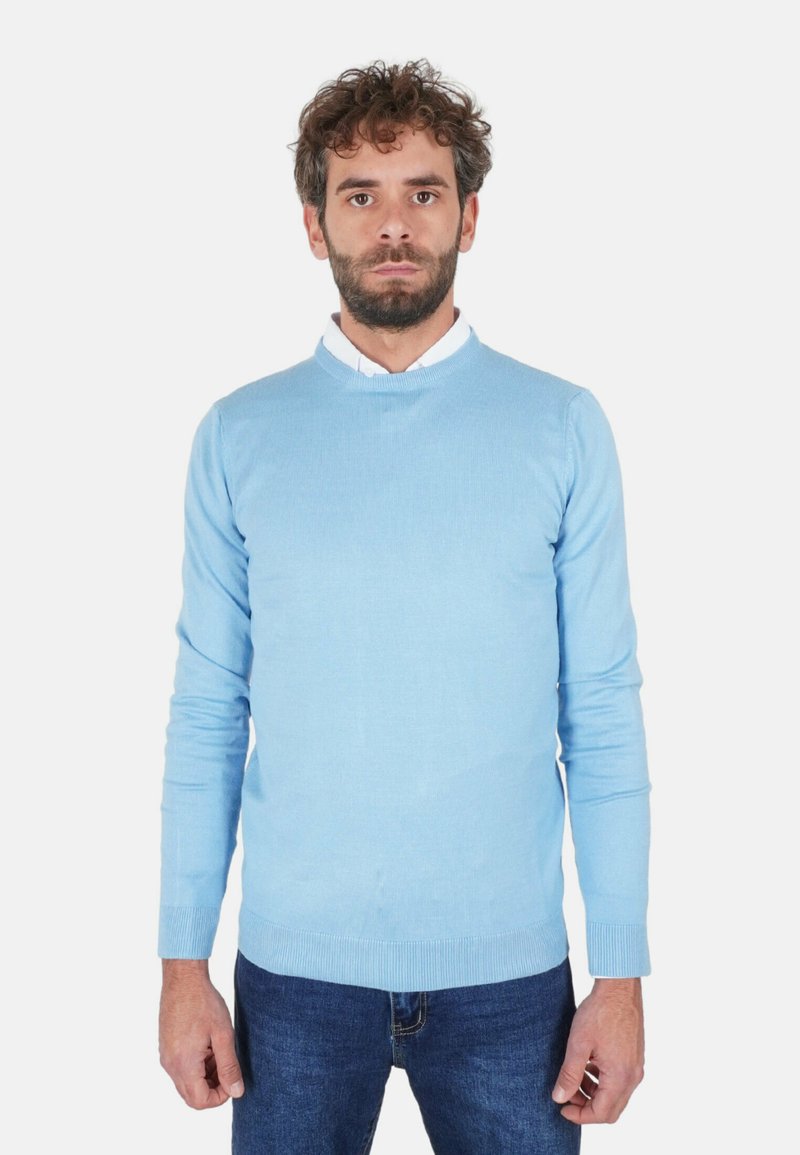 Maglione azzurro chiaro in maglia con scollo rotondo, polsini e orlo a coste. Indossato sopra una camicia bianca con colletto, abbinato a jeans blu scuro.
