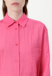 Rosa Hemd mit Knopfleiste und strukturiertem Finish, ausgestattet mit einem Kragen, einer Brusttasche und subtiler Markenkennung im Taschenbereich.