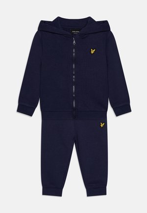 Marineblauwe trainingsset, met een rits hoodie van een zachte stof en een opvallend geel logo, gecombineerd met bijpassende joggingbroek.