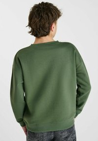 Groene sweatshirt met een ronde hals en geribde manchetten. De stof lijkt zacht, met een gladde textuur en een relaxte pasvorm.