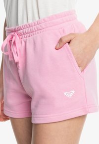 Růžové bavlněné šortky s elastickým pasem, detailem v podobě stahovací šňůrky a bočními kapsami. Na dolním lemu mají malé bílé logo.