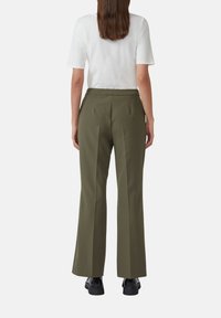 Pantaloni su misura verde oliva con design a gamba dritta e pieghe posteriori, abbinati a una maglietta bianca a maniche corte e scarpe nere.