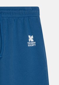 Shorts di cotone blu con una texture morbida, cintura elastica e logo bianco "THE NEW SOCIETY" stampato sul lato sinistro in basso.