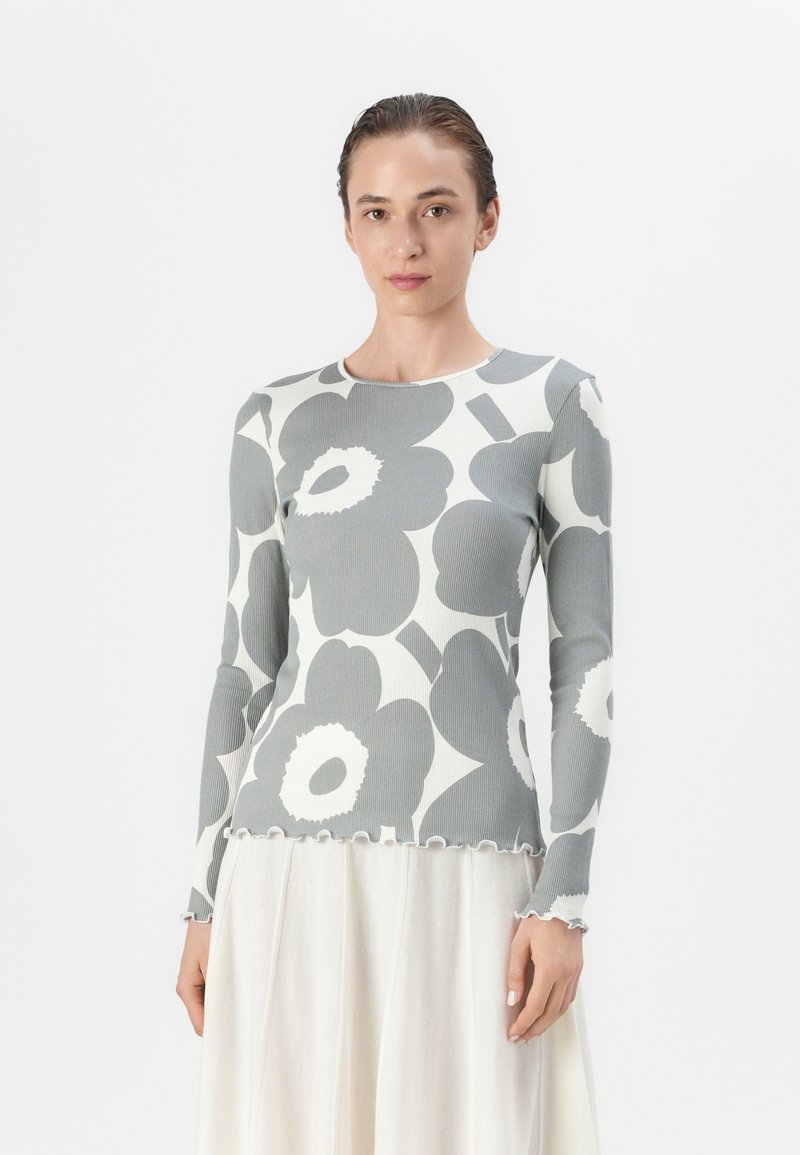 Ribbestrikket langermet topp i grått med bold hvite blomster mønstre, rund halslinje og bølgete kant. Kombinert med en lett, skinnende skjørt.