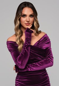 Sammetklänning i djupt lila med off-shoulder-design, långa ärmar och rynkdetaljer. Slät textur med figurnära silhuett.