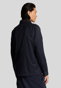 Giacca leggera di colore blu navy con colletto classico e maniche lunghe. Texture liscia e design semplice, caratterizzata da un taglio dritto e accenti minimi.