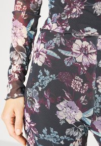 Body de flores com uma base preta, mangas longas transparentes e padrões vibrantes de flores em roxo, rosa e azul, com um acabamento texturizado.