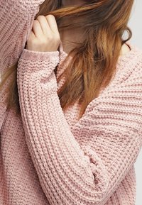 Helles rosa Strickpullover mit lockerer Passform und strukturiertem Muster, ausgestattet mit langen Ärmeln und einem weiten Ausschnitt. Weiches, lässiges Design.
