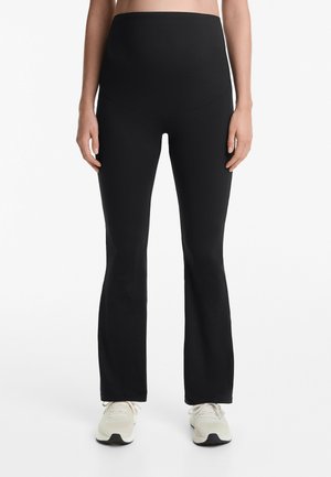 Leggings neri a vita alta con una texture liscia, design svasato e una cintura senza cuciture, abbinate a scarpe da ginnastica chiare.