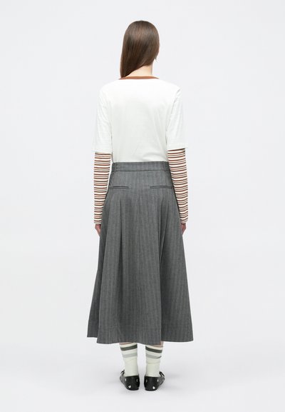 Λευκό κορυφαίο με κοντά μανίκια πάνω από ριγέ πουκάμισο με μακριά μανίκια, σε συνδυασμό με γκρι πλισέ midi φούστα και πράσινες ριγέ κάλτσες, φορεμένα με μαύρα ξώφτερνα.