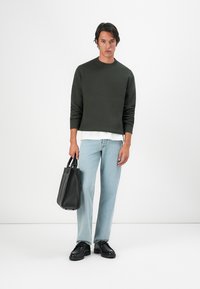 Mörkgrön stickad tröja, ljusblå raka jeans, svart handväska och svarta skor. Enkelt design med texturerad tyg.