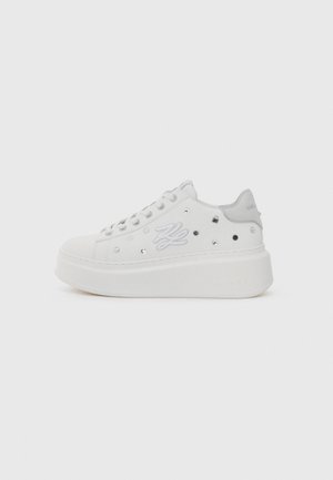 Zapatillas blancas tipo plataforma con un material suave, tachuelas decorativas en plata y una marca bordada en el lateral.