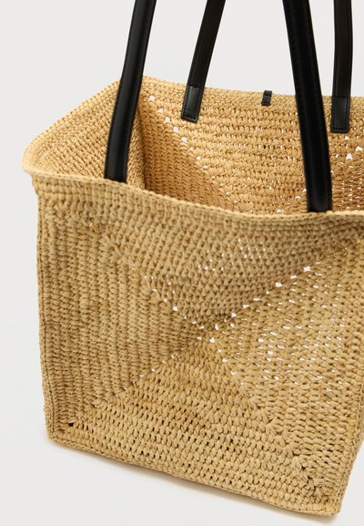 Πλεκτή τσάντα ώμου από ψάθα με μαύρες δερμάτινες λαβές, ευρύχωρο ανοιχτό πάνω μέρος και υφή με σχέδιο στο σώμα.