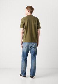 Oliven grøn T-shirt med rund hals, parret med lyseblå lige bukser med to baglommer og en falmet tekstur.