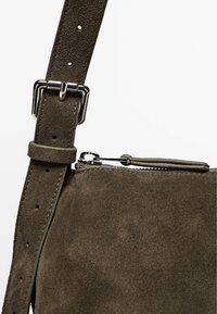 Borsa a tracolla in suede verde oliva scuro con zip in tonalità argento e tracolla regolabile con più fori per personalizzare la misura.