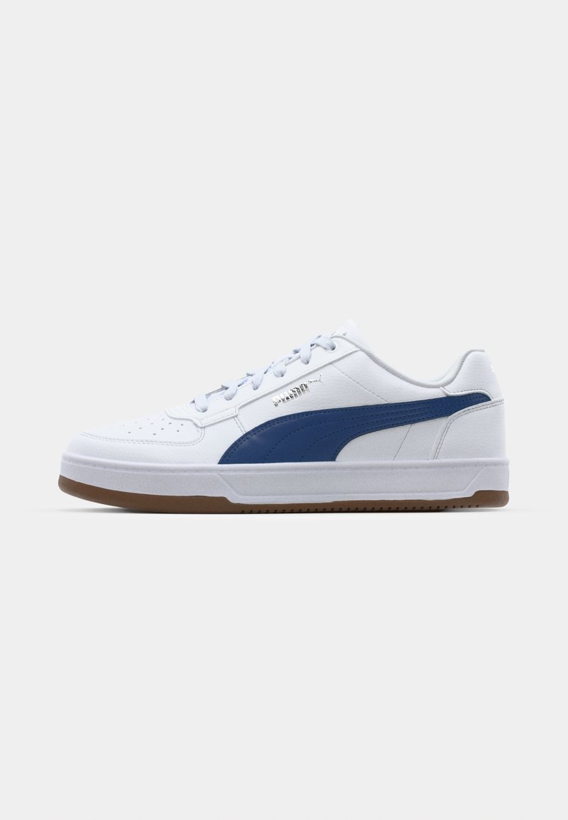 Sneaker de sport blanche avec des accents bleus, en cuir texturé, avec un bout perforé, des lacets plats et une semelle en caoutchouc naturel. Présente un logo sur le côté.