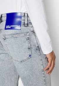 Ljusblå denimjeans med en blå läderlogotyp på bakfickan. Har standardfickor och subtila blekningsdetaljer.
