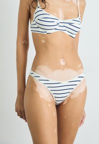 Striped bikini set in cream and navy, featuring a simple design with thin straps and a low-rise bottom. Fabric appears smooth and stretchy.