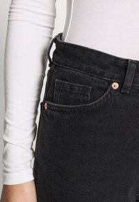 Vaqueros de mezclilla negra con un diseño clásico, que cuentan con un bolsillo frontal, detalles de herrajes de cobre y un acabado texturizado.