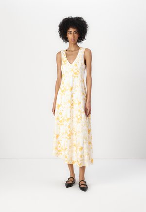 Weißes ärmelloses Kleid mit gelbem Blumenmuster, V-Ausschnitt und A-Linie, kombiniert mit schwarzen Ballerinas. Glatte Stofftextur.