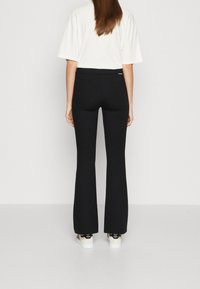 Zwarte flared broek gemaakt van rekbare stof, met een hoge tailleband, gecombineerd met een losse witte shirt met ronde hals.