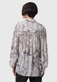 Lettet, gennemsigtig bluse i off-white med grå blomstermotiv. Har lange æermer, gathered ryg og en blød, tekstureret overflade.