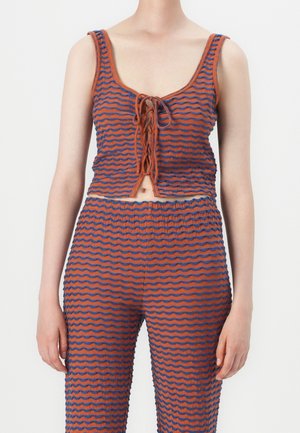 Kvinde iført orange og blå bølget stribet ærmeløs crop top med frontknude og matchende bukser med høj talje.