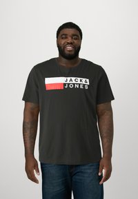 Black short-sleeve t-shirt featuring a white and red horizontal block graphic with "JACK&JONES" text in bold, contrasting white letters.