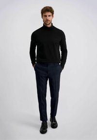 Zwarte langemouwen coltrui, slim fit. Marineblauwe broek met ruitpatroon en een getailleerde pasvorm. Zwarte veterschoenen maken de outfit compleet.