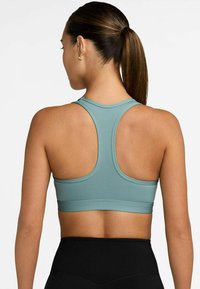 Un sujetador deportivo en color verde azulado con un diseño de espalda nadadora, hecho de una tela suave, que presenta una banda ancha en la parte inferior y detalles de costura mínimos.