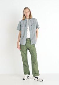 Gray short-sleeve shirt with chest pockets, white t-shirt underneath, olive green cargo pants, and black/white sneakers. Smooth fabric, relaxed fit.