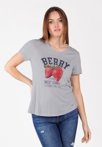 Camiseta gris hecha de material suave con un gráfico de fresas y texto. Cuello redondo y mangas cortas con un ajuste relajado.