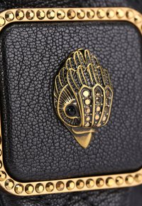 Czarna, teksturowana skóra z złotym elementem dekoracyjnym, zawierającym misternie wykonane detale i kryształki wzdłuż krawędzi.