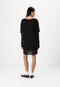 Fekete ruha rövid ujjú felsőrésszel és hosszú csipkés ujjak, áttetsző csipke szegéllyel. A fazon laza illeszkedésű és kerek nyakú.