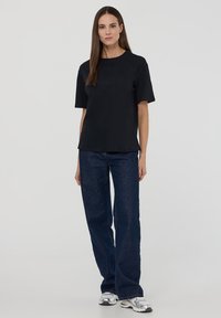 Czarny t-shirt z krótkim rękawem i okrągłym dekoltem, zestawiony z szerokimi granatowymi dżinsami i srebrnymi butami sportowymi. Prosty design, gładka tekstura.