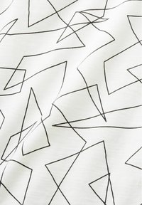 Tissu blanc avec des motifs de lignes géométriques abstraites noires et irrégulières formant des triangles et diverses formes angulaires.