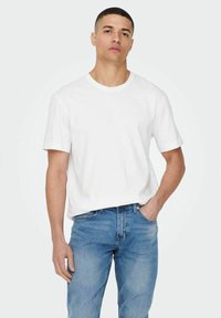 White cotton t-shirt with short sleeves, crew neck, and relaxed fit, paired with blue denim jeans. Simple design, no patterns or accents.