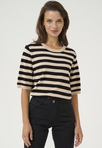 Un pull en tricot rayé crème et noir avec un col rond côtelé, des manches courtes et une coupe décontractée, associé à un jean noir ajusté.