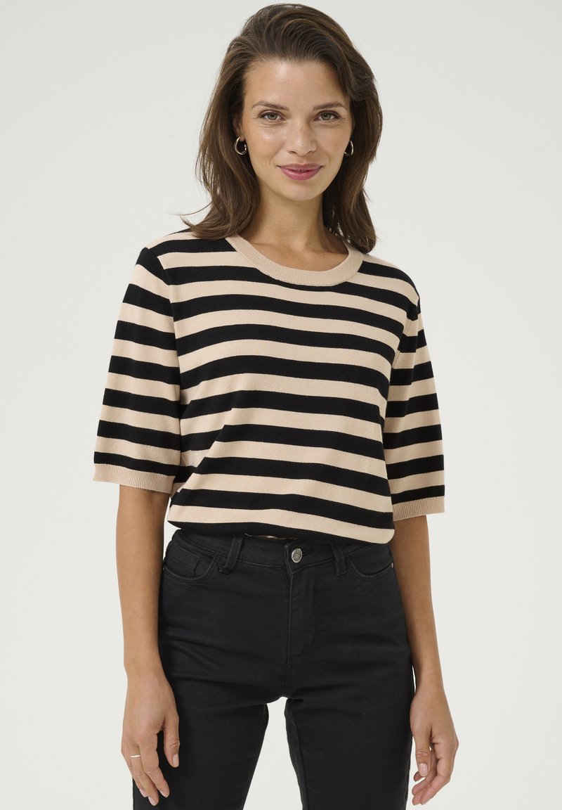 Un pull en tricot rayé crème et noir avec un col rond côtelé, des manches courtes et une coupe décontractée, associé à un jean noir ajusté.