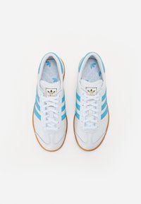 Zapatillas blancas con rayas azul claro, suela de goma texturizada y un acento de logo dorado en la lengüeta. Parte superior de cuero suave.