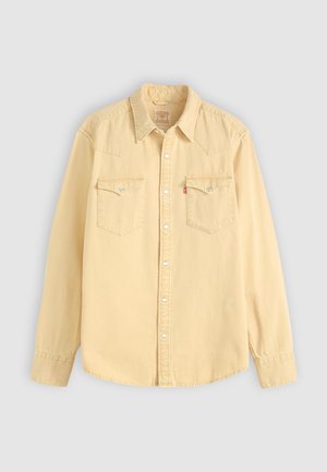 Beige long-sleeve denim shirt with pointed collar, snap buttons, and two chest flap pockets with metal snaps.
