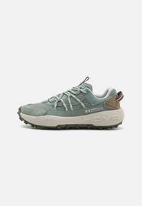 Scarpe da trekking verde chiaro con tomaia texture, accenti in suede e suola chunky di color crema. Presentano lacci riflettenti e un tab in pelle marrone sul tallone.
