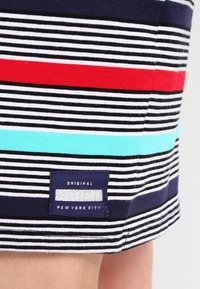 Gestreepte stof met horizontale lijnen in zwart, wit, rood en teal. Bevat een blauwe label met witte tekst met de opdruk "Original Superdry New York City."