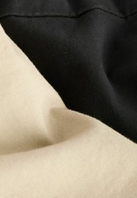Twee stukken stof: é�én zwarte, gestructureerde katoen en één beige, gladde katoen. De stoffen zijn gevouwen, waardoor de contrasterende kleuren en texturen zichtbaar zijn.