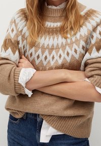 Beige Pullover mit geometrischem weißen und braunen Muster, Rundhalsausschnitt, gerippte Bündchen und Saum, über einem weißen Hemd getragen, strukturierter Strickstoff.